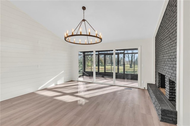 unfurnished living room with a chandelier, vaulted ceiling, hardwood / wood-style flooring, and a brick fireplace