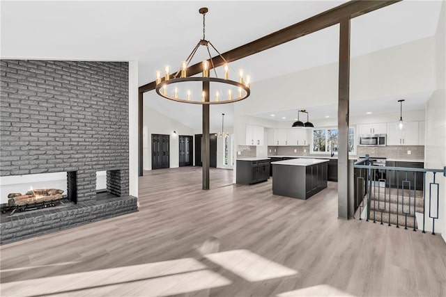 living room featuring vaulted ceiling with beams, light hardwood / wood-style flooring, a fireplace, and an inviting chandelier