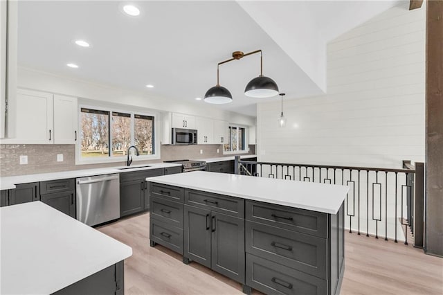 kitchen with white cabinetry, sink, pendant lighting, a kitchen island, and appliances with stainless steel finishes