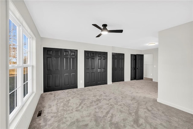 unfurnished bedroom featuring ceiling fan, carpet, and two closets