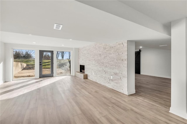 unfurnished living room with a barn door, a fireplace, and light hardwood / wood-style floors