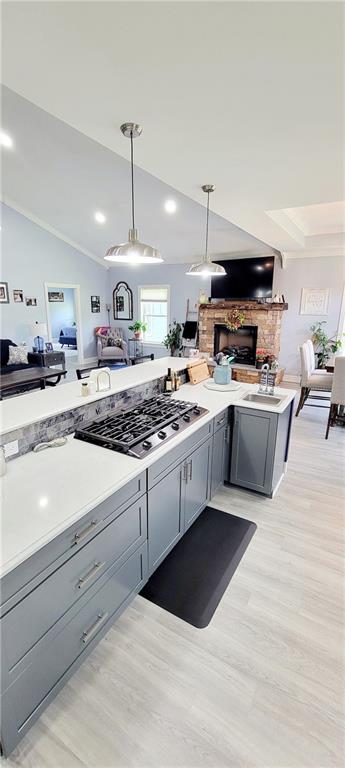 kitchen featuring stainless steel gas cooktop, light wood-type flooring, gray cabinets, pendant lighting, and lofted ceiling