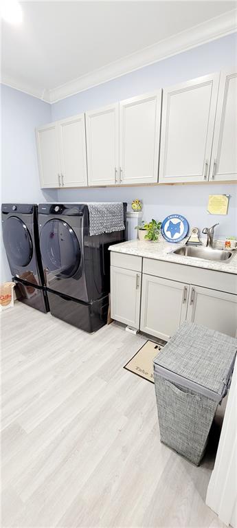 laundry room with separate washer and dryer, crown molding, light wood-type flooring, cabinets, and sink