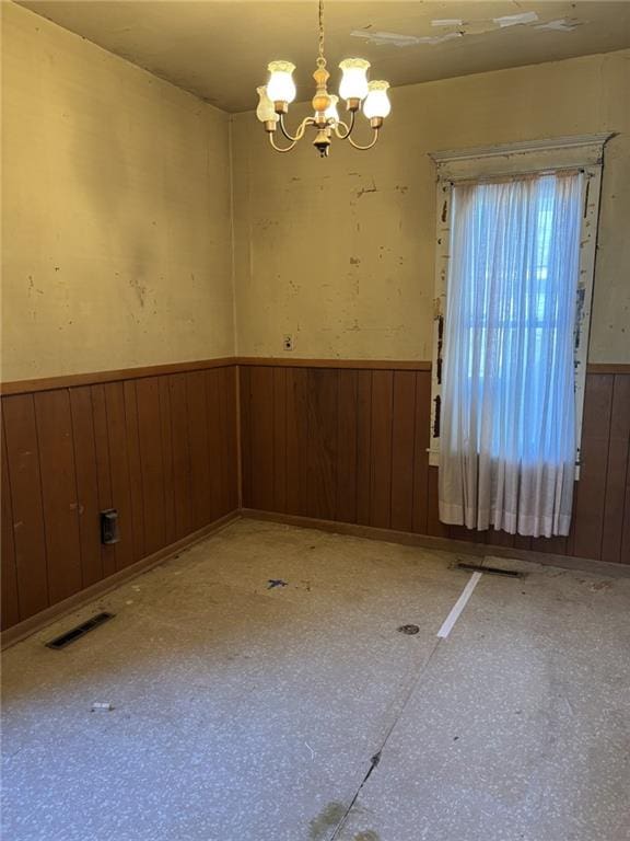 spare room with an inviting chandelier and wooden walls