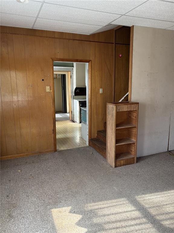 empty room featuring a drop ceiling, wooden walls, and light colored carpet