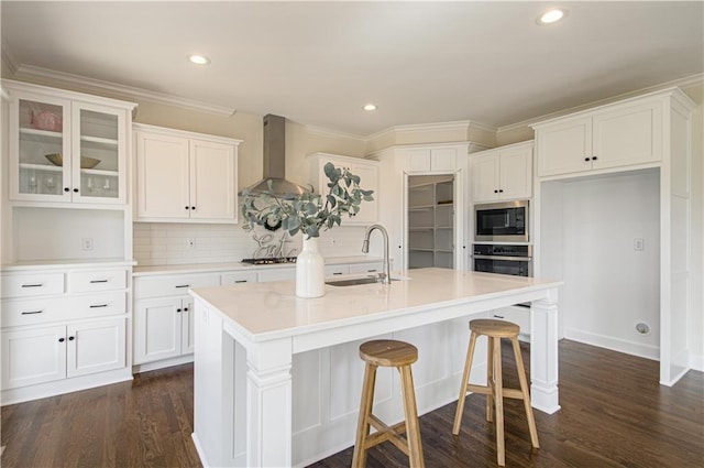 kitchen featuring sink, wall chimney exhaust hood, an island with sink, white cabinetry, and stainless steel appliances