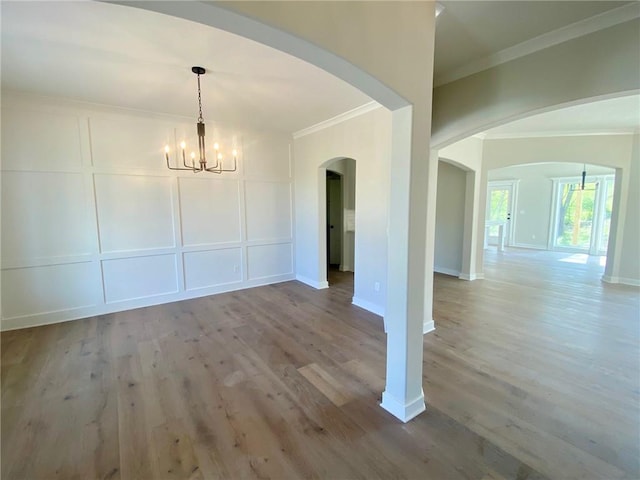 unfurnished dining area featuring arched walkways, an inviting chandelier, wood finished floors, a decorative wall, and ornamental molding