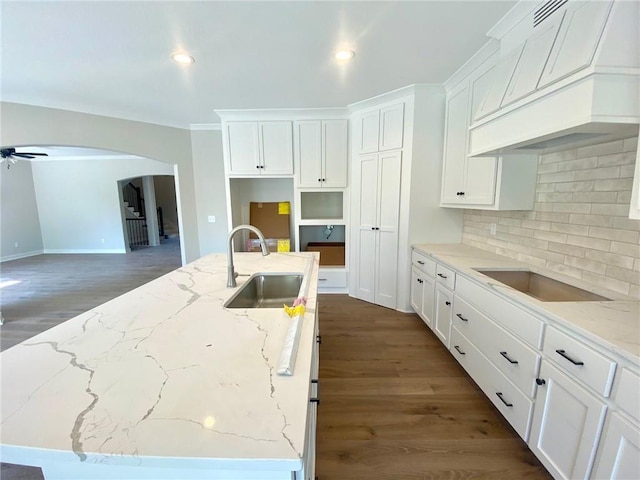 kitchen with tasteful backsplash, a sink, arched walkways, custom range hood, and dark wood-style floors
