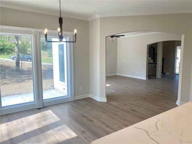 unfurnished dining area featuring wood finished floors, visible vents, arched walkways, crown molding, and baseboards