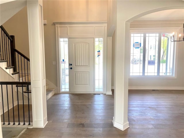 entrance foyer with arched walkways, dark wood-style flooring, baseboards, stairway, and ornamental molding