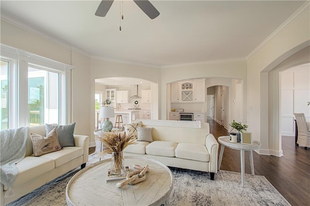 living area with crown molding, ceiling fan, arched walkways, baseboards, and dark wood-style flooring
