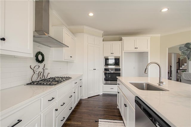 kitchen featuring white cabinets, stainless steel appliances, wall chimney range hood, a sink, and light stone countertops