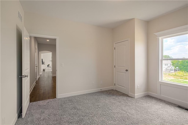 unfurnished room with arched walkways, carpet floors, visible vents, and baseboards