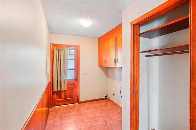 clothes washing area with cabinets, wooden walls, and a textured ceiling