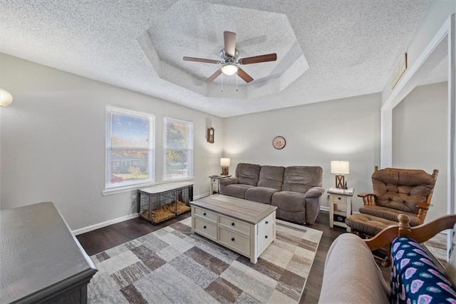 living room with a raised ceiling, ceiling fan, dark hardwood / wood-style floors, and a textured ceiling