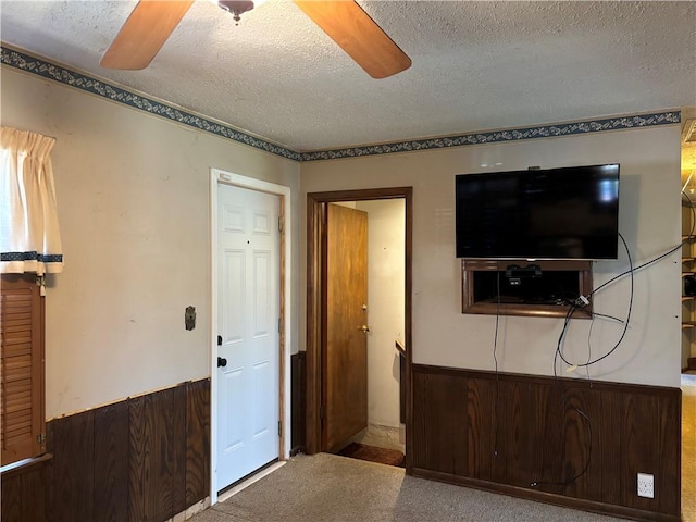 interior space featuring wooden walls, a textured ceiling, ceiling fan, and carpet flooring