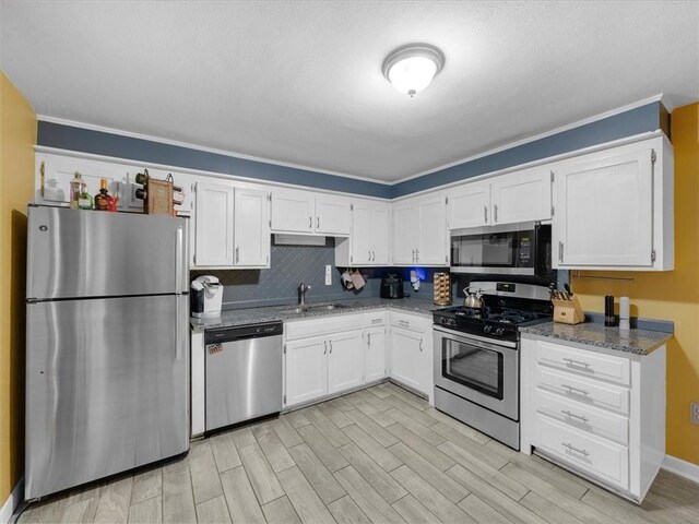 9317 Gillette St, Lenexa, KS 66215 - kitchen with stainless steel appliances, white cabinetry, light wood finished floors, stone counters, and a textured ceiling