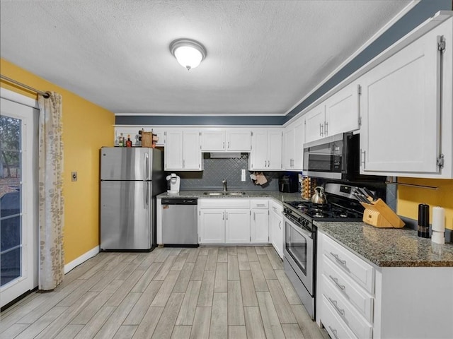9317 Gillette St, Lenexa, KS 66215 - kitchen with appliances with stainless steel finishes, white cabinets, light wood-style flooring, dark stone counters, and a textured ceiling