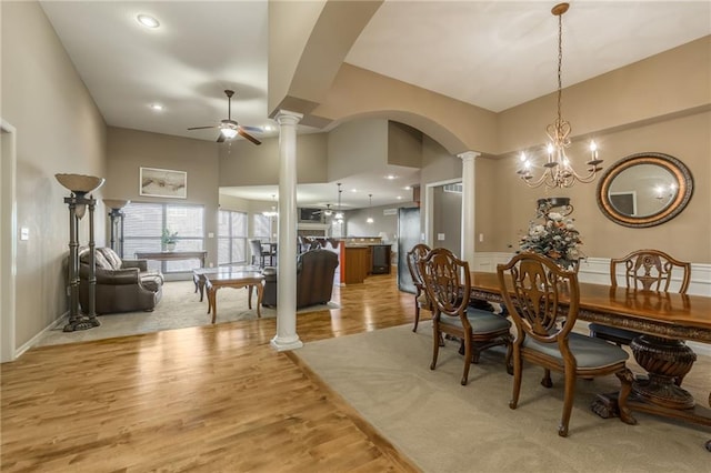 dining room with ceiling fan with notable chandelier, light wood-type flooring, a high ceiling, and ornate columns