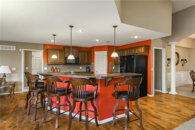 kitchen featuring dark hardwood / wood-style floors, pendant lighting, decorative columns, a breakfast bar area, and black appliances