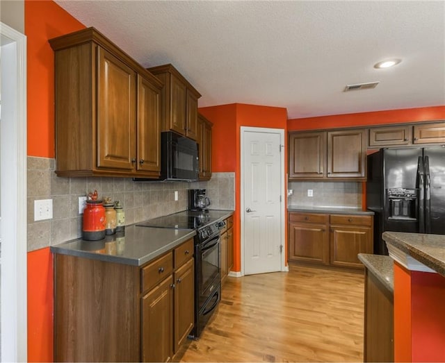 kitchen featuring backsplash, light hardwood / wood-style floors, a textured ceiling, and black appliances