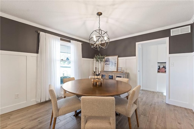 dining area with light hardwood / wood-style floors, crown molding, and an inviting chandelier