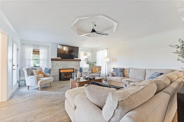 living room featuring ceiling fan, crown molding, light wood-type flooring, and a fireplace