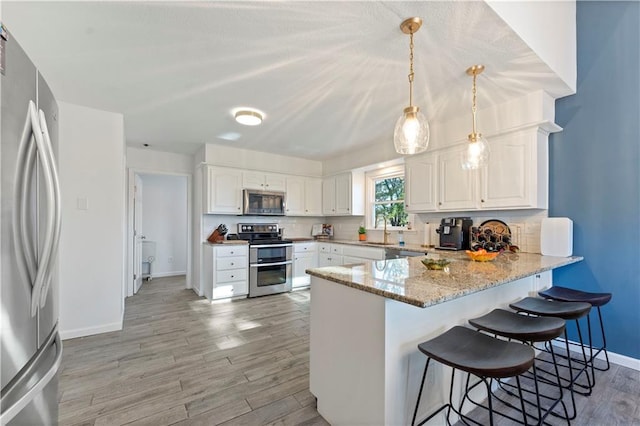 kitchen with sink, hanging light fixtures, kitchen peninsula, white cabinets, and appliances with stainless steel finishes