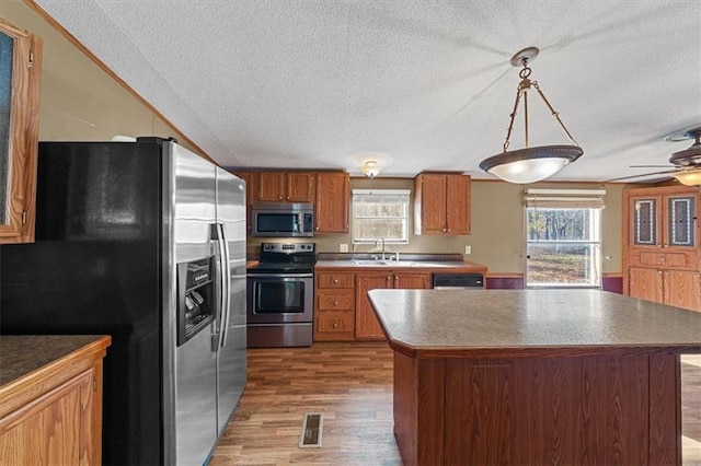 kitchen with hanging light fixtures, sink, hardwood / wood-style flooring, appliances with stainless steel finishes, and a kitchen island