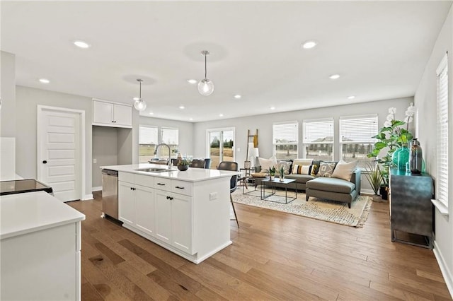 kitchen featuring sink, decorative light fixtures, a center island with sink, dishwasher, and white cabinetry