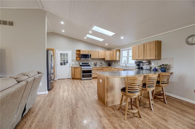 kitchen with kitchen peninsula, appliances with stainless steel finishes, light brown cabinetry, a kitchen breakfast bar, and light hardwood / wood-style floors