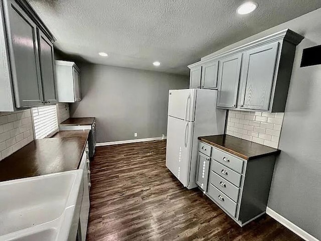 kitchen featuring gray cabinetry, dark wood-type flooring, white refrigerator, a textured ceiling, and decorative backsplash