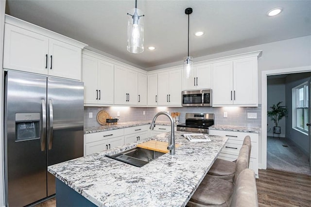 kitchen with sink, hanging light fixtures, an island with sink, stainless steel appliances, and white cabinets