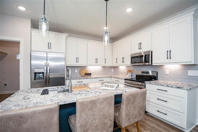 kitchen featuring a breakfast bar, a center island with sink, appliances with stainless steel finishes, pendant lighting, and white cabinets