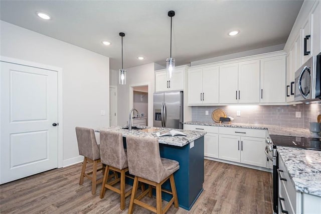 kitchen with appliances with stainless steel finishes, decorative light fixtures, an island with sink, white cabinets, and light stone countertops