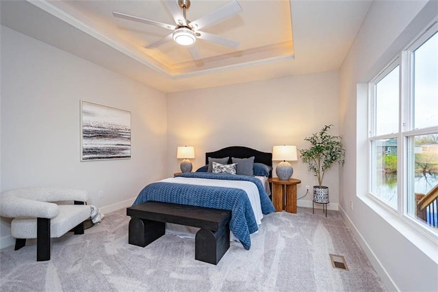 carpeted bedroom with multiple windows, a tray ceiling, and ceiling fan