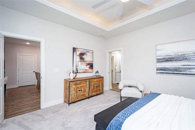 carpeted bedroom with a raised ceiling, ensuite bathroom, and ceiling fan