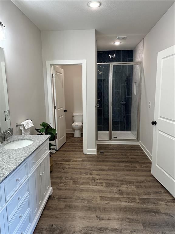 bathroom featuring walk in shower, vanity, toilet, and hardwood / wood-style floors