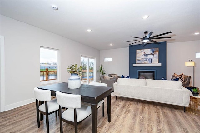 dining space with a large fireplace, light wood-style flooring, a ceiling fan, baseboards, and recessed lighting