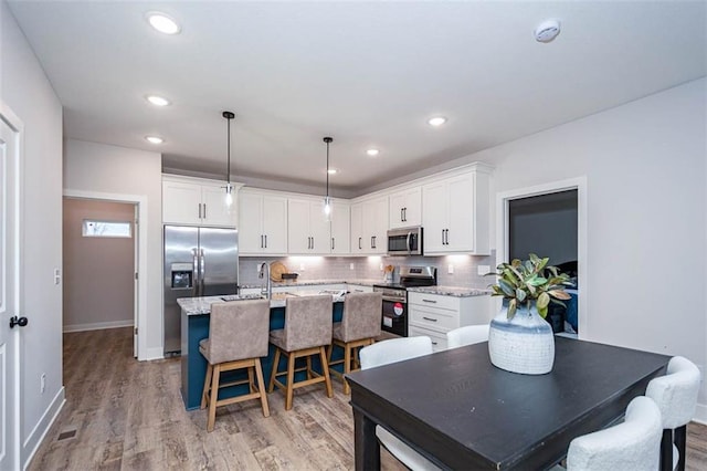 kitchen with decorative backsplash, stainless steel appliances, white cabinetry, and an island with sink