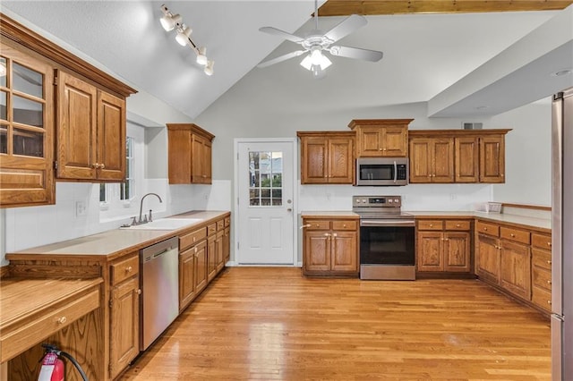 kitchen with light wood-type flooring, stainless steel appliances, vaulted ceiling, ceiling fan, and sink