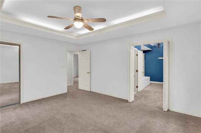 unfurnished bedroom with a tray ceiling, ceiling fan, crown molding, and light carpet