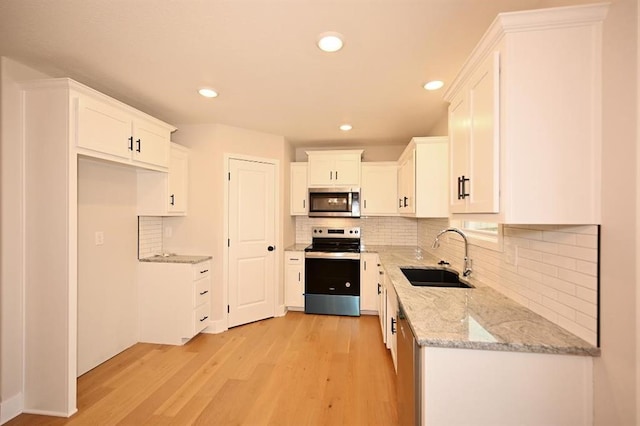 kitchen featuring sink, light stone counters, stainless steel appliances, light hardwood / wood-style floors, and white cabinets