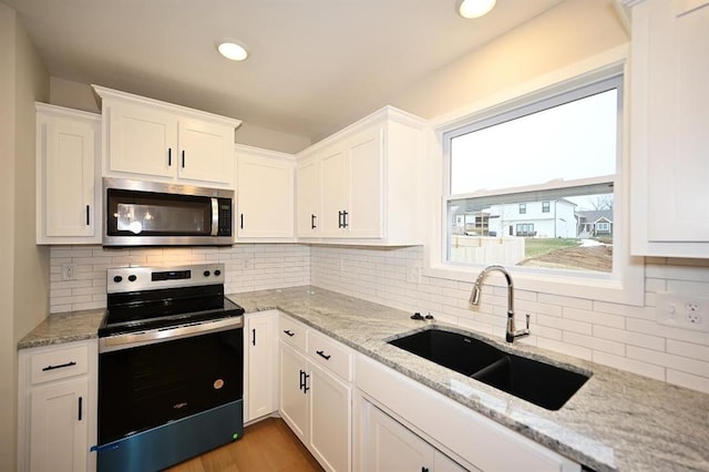 kitchen with sink, white cabinetry, stainless steel appliances, light stone counters, and decorative backsplash