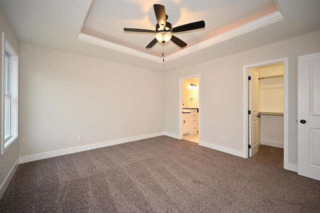 unfurnished bedroom featuring ornamental molding, a spacious closet, a raised ceiling, and dark colored carpet