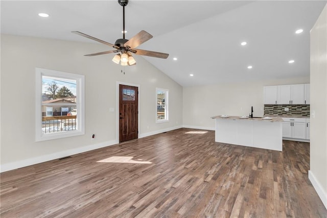 unfurnished living room with hardwood / wood-style flooring, vaulted ceiling, sink, and ceiling fan