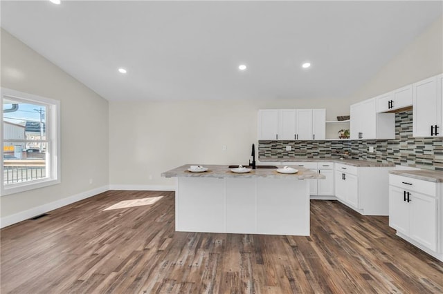 kitchen featuring tasteful backsplash, white cabinetry, lofted ceiling, light stone counters, and a center island with sink