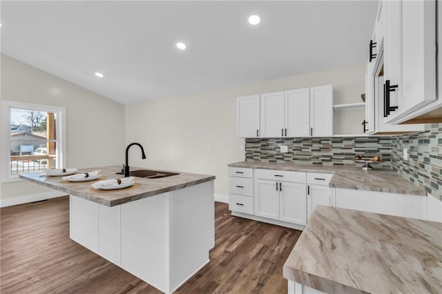 kitchen with vaulted ceiling, white cabinetry, sink, decorative backsplash, and a center island with sink