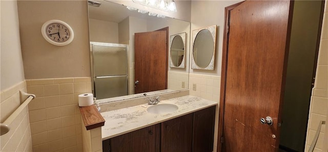 bathroom with vanity, a shower with door, and tile walls