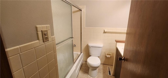 bathroom with tile patterned floors, enclosed tub / shower combo, tile walls, and toilet